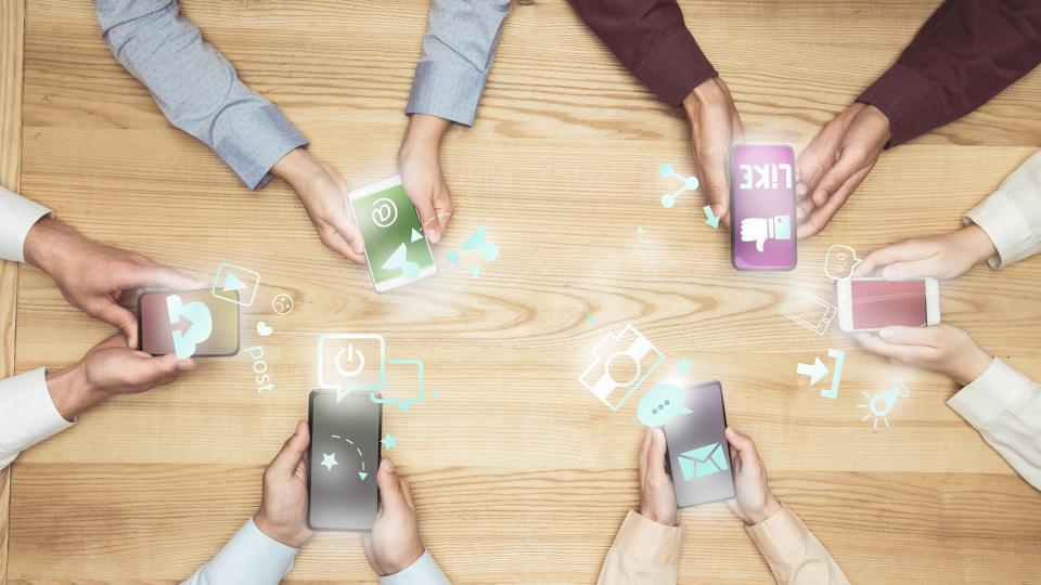 Stockfoto - Draufsicht auf Geschäftsleute bei Treffen über soziale Medien auf Smartphones auf hölzerner Tischplatte