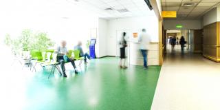 Stock Photo - View of the registration desk waiting area and a corridor in modern hospital with blurred figures of patients with a copy space.